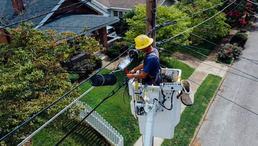 Electrician in a bucket lift repairing power lines from a utility pole in a suburban neighborhood