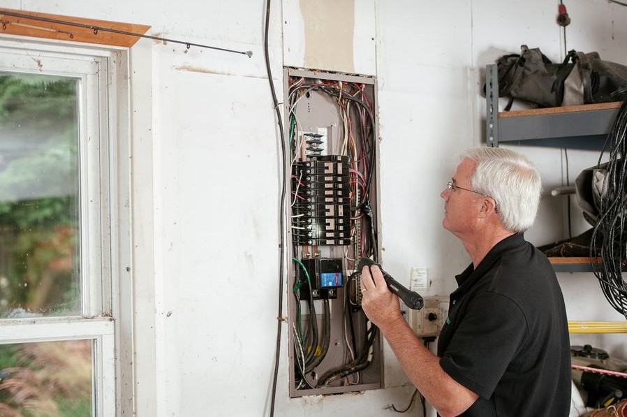 An electrician carefully examines a residential fuse box indoors, ensuring electrical safety and compliance